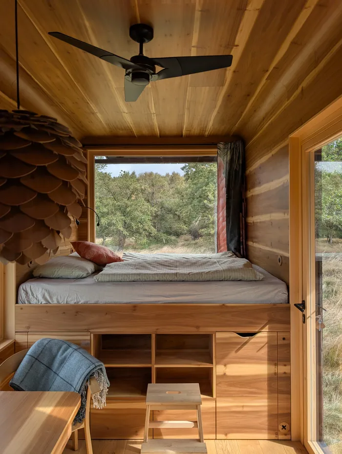 Postel u velkého okna v interiéru tiny house U Lesa