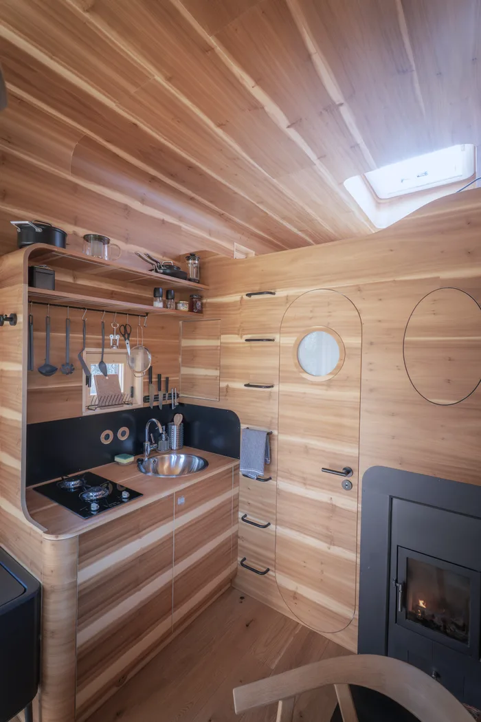 Kuchyňka s plynovým vařičem, dřezem a kamny v dřevěném interiéru tiny house U Lesa