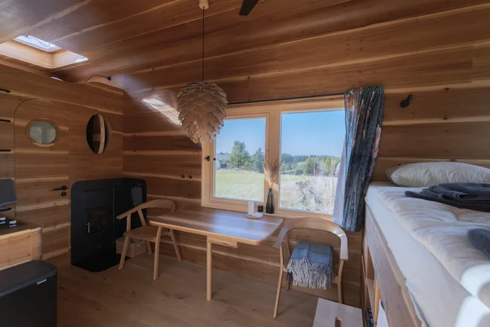 Interiér tiny house U Lesa s jídelním stolem u okna, kamny a postelí