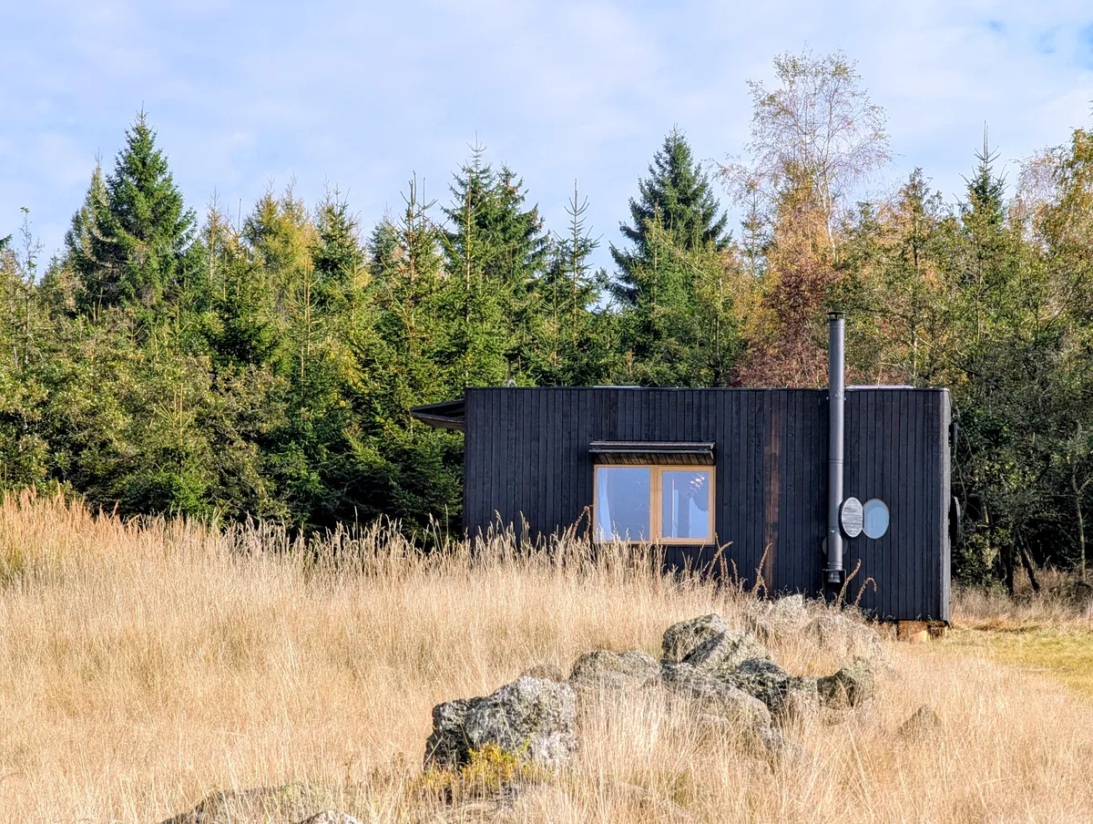 Tiny house U Lesa na podzimní louce s kameny před smrkovým lesem